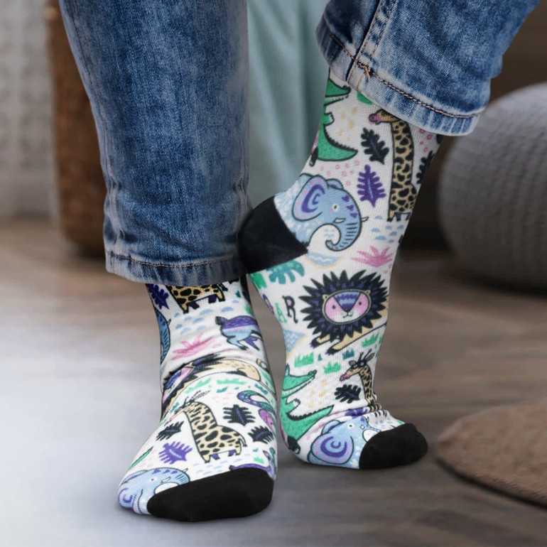 Colourful crew socks featuring playful animal patterns, with a black toe and heel, worn by a person in denim jeans.