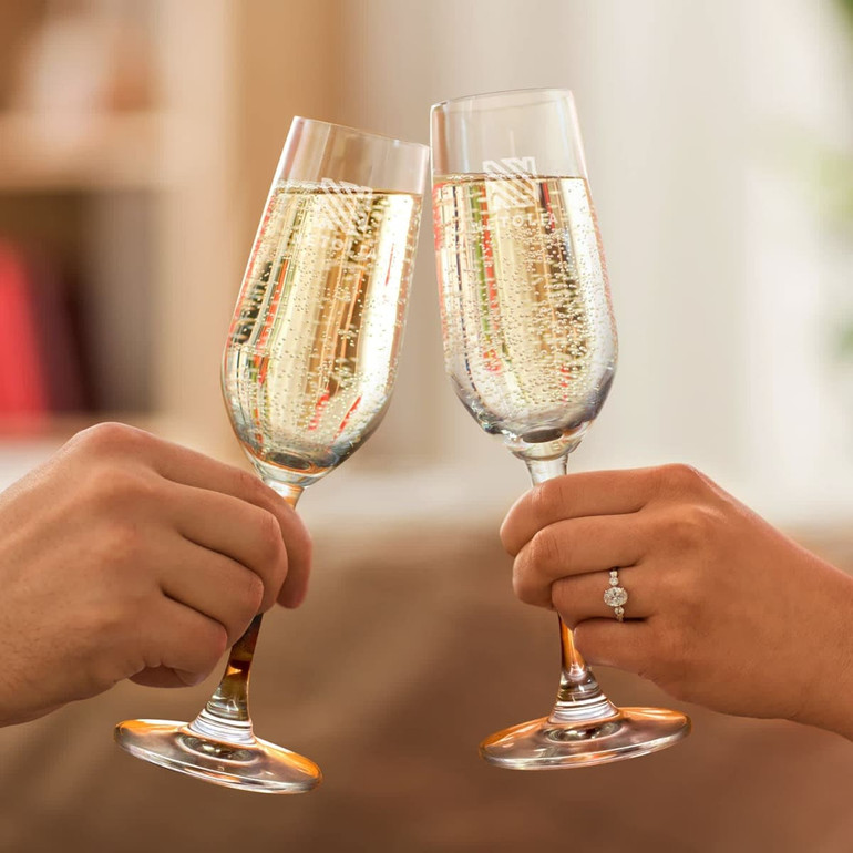 Two elegant glass champagne flutes filled with bubbly champagne, clinking together. Both glasses have a logo.