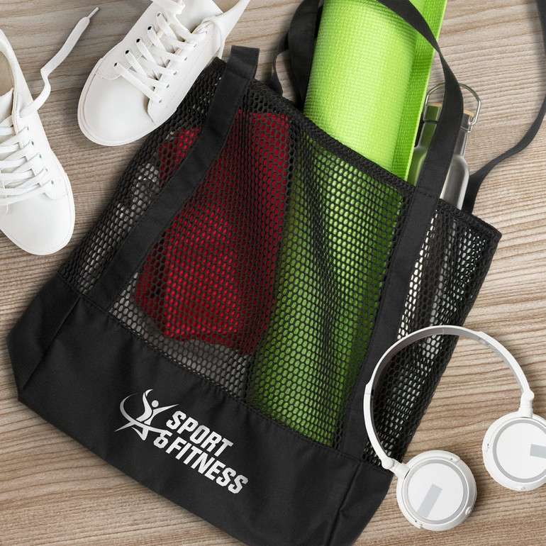 A black mesh tote bag containing a red item, a green yoga mat, white sneakers, and white headphones.