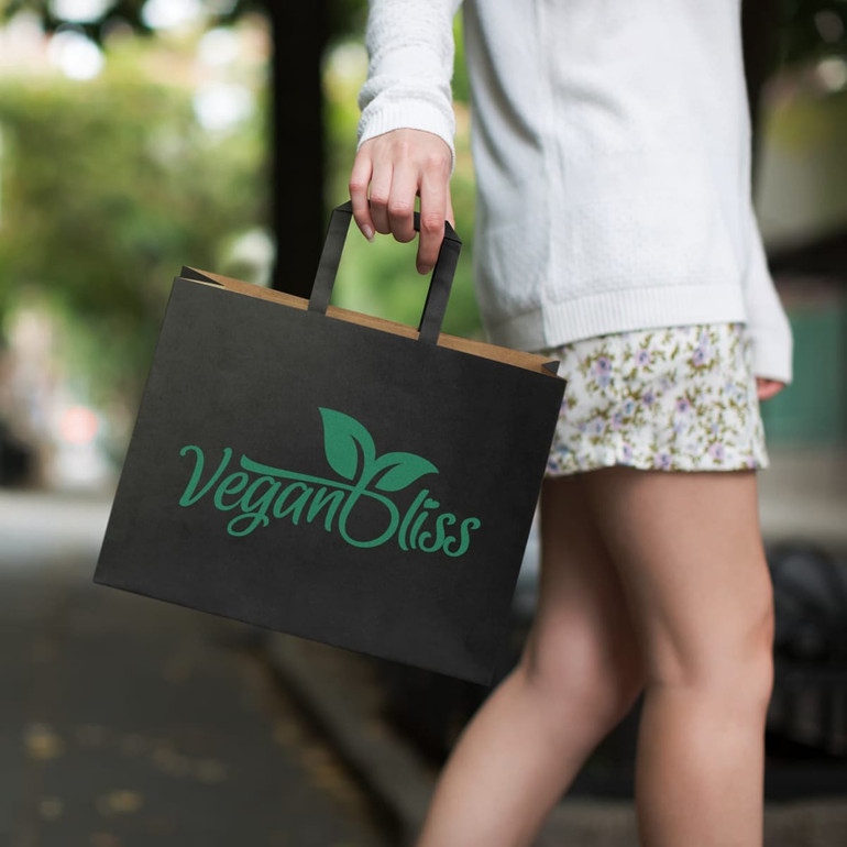 A large black flat handle paper bag with a green logo is being held by a person walking outdoors.