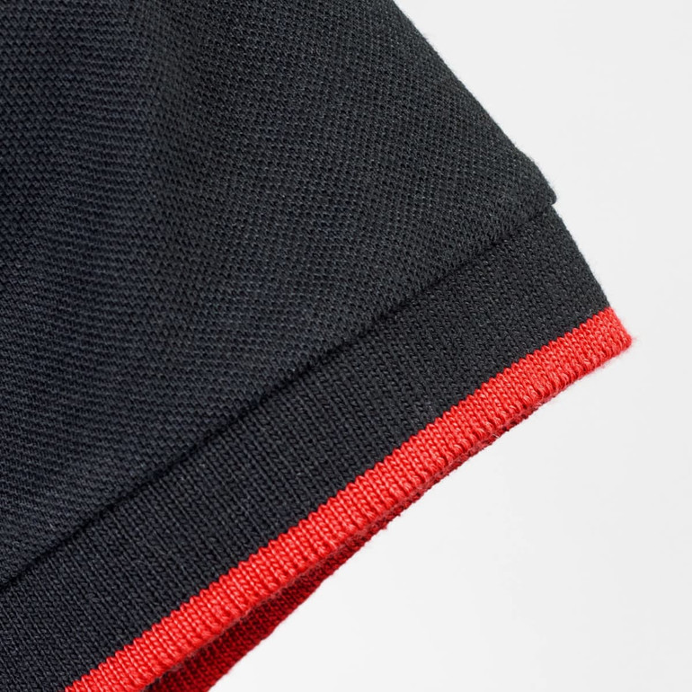 A black polo shirt featuring a red trim on the collar and sleeve. It has a branding logo.