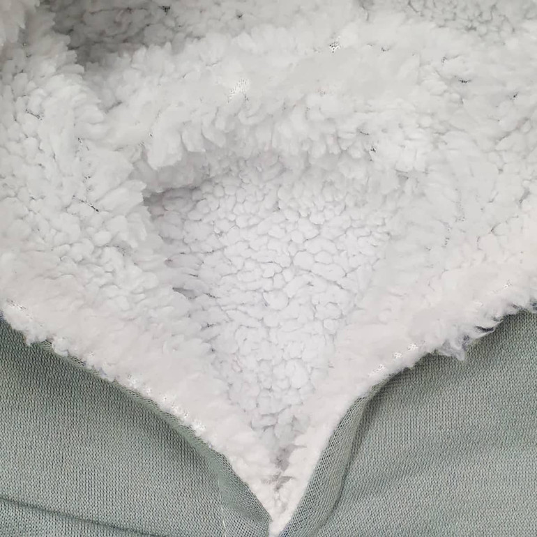 A detail of a soft, fluffy inner lining in a hoodie, featuring grey outer material and textured white fleece.