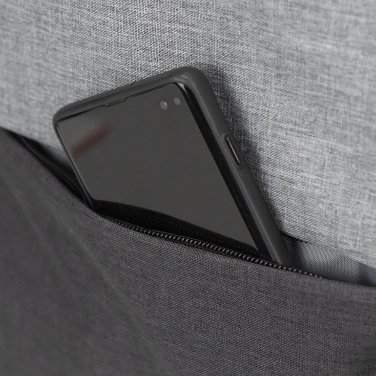 A smartphone in a grey fabric pocket of a black backpack with a zip.