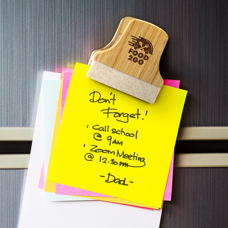 A bamboo clip holding several colourful sticky notes on a fridge, featuring a smooth finish and a logo.