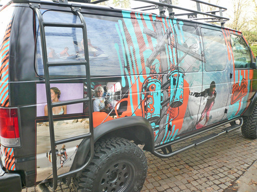 A mural-wrapped Ford E-series van with a set of nerf bars from Aluminess Products.