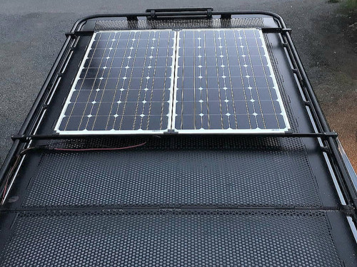 Aluminess roof rack with adjustable solar panel mounts on a Chevy Express van.