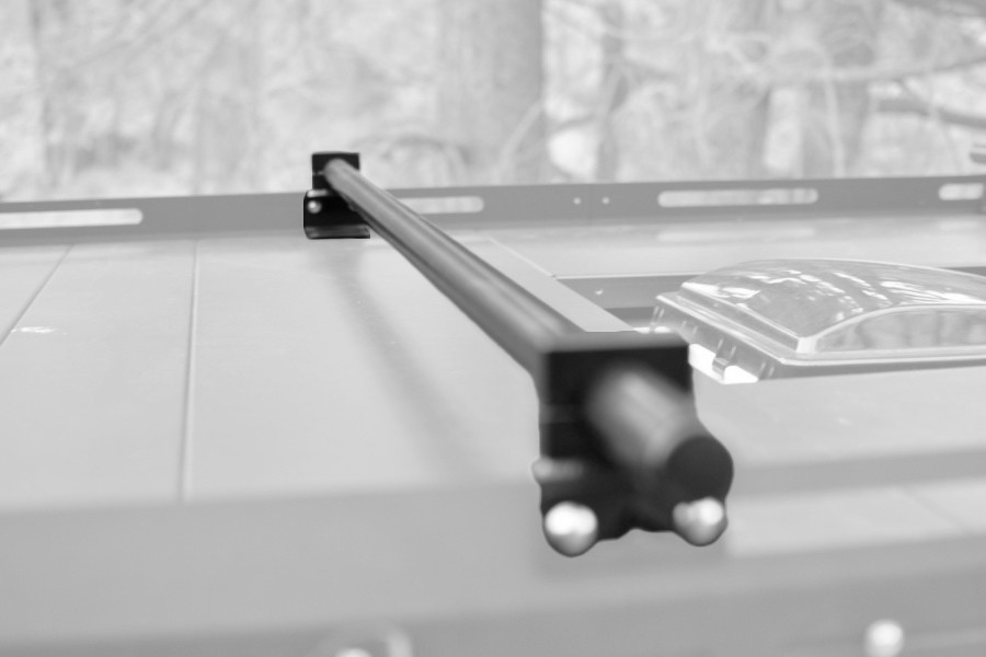 Close-up view of a black roof rack crossbar installed on a Sprinter van, with a blurry background.