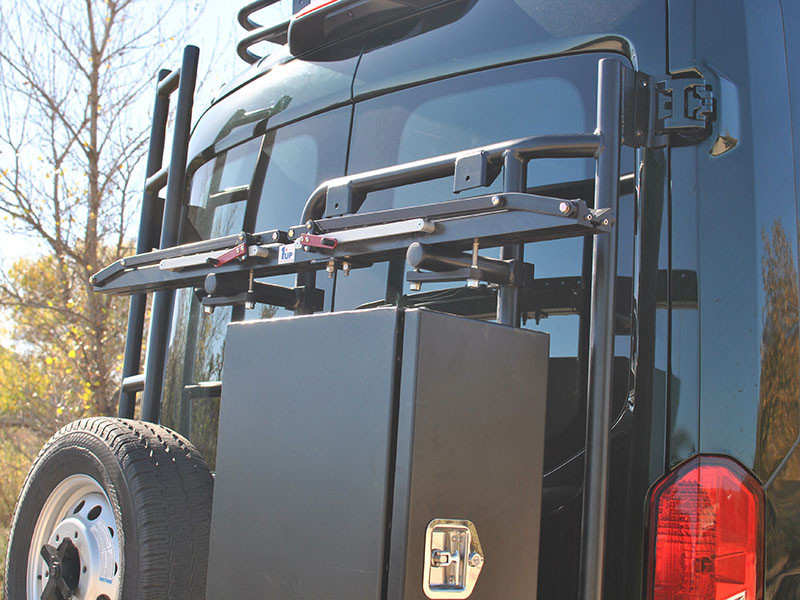 A black Ford Transit van with a tire carrier and rear door bike rack.