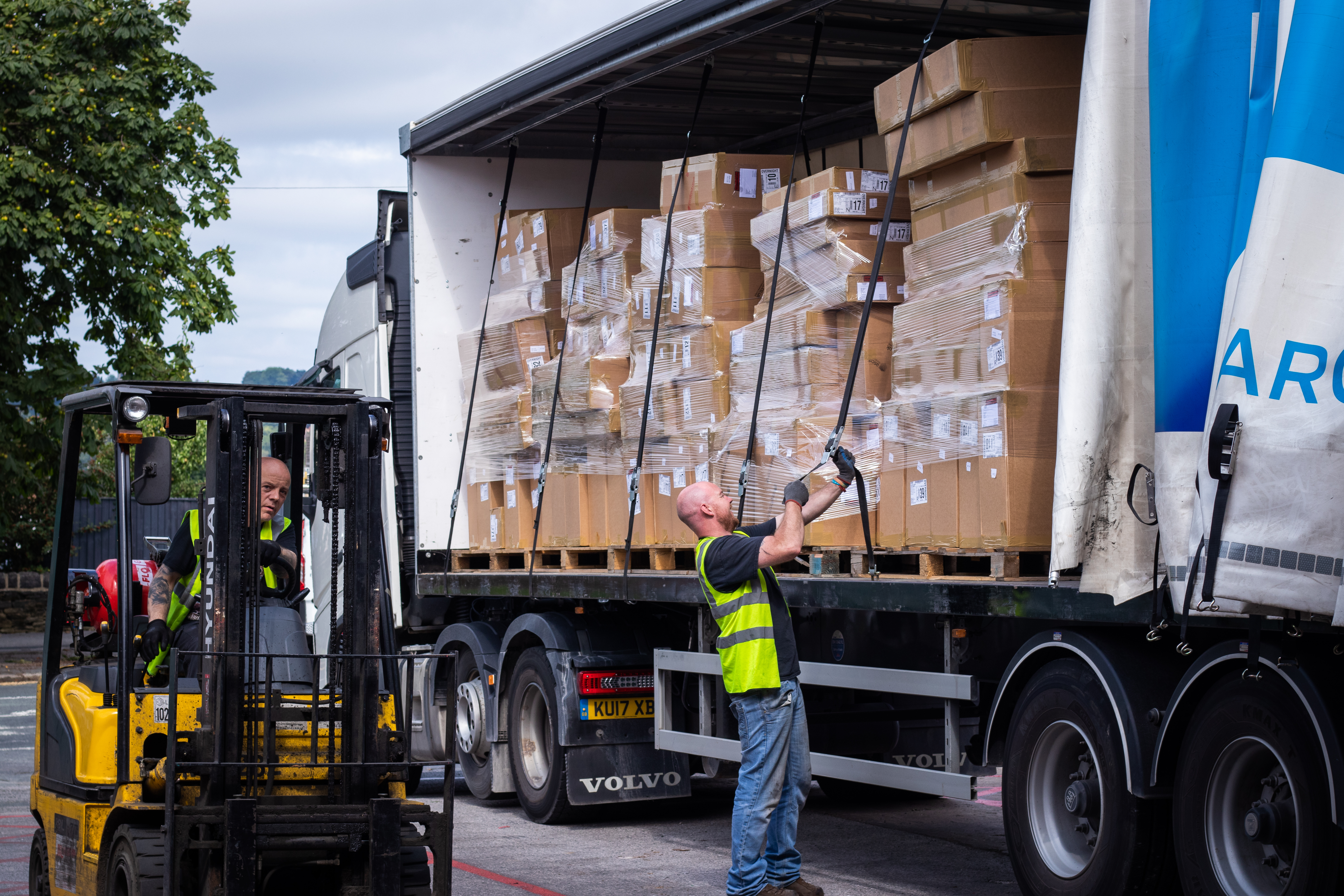 ASC Direct staff member driving forklift while courier ties down straps on the delivery lorry full of packed boxes