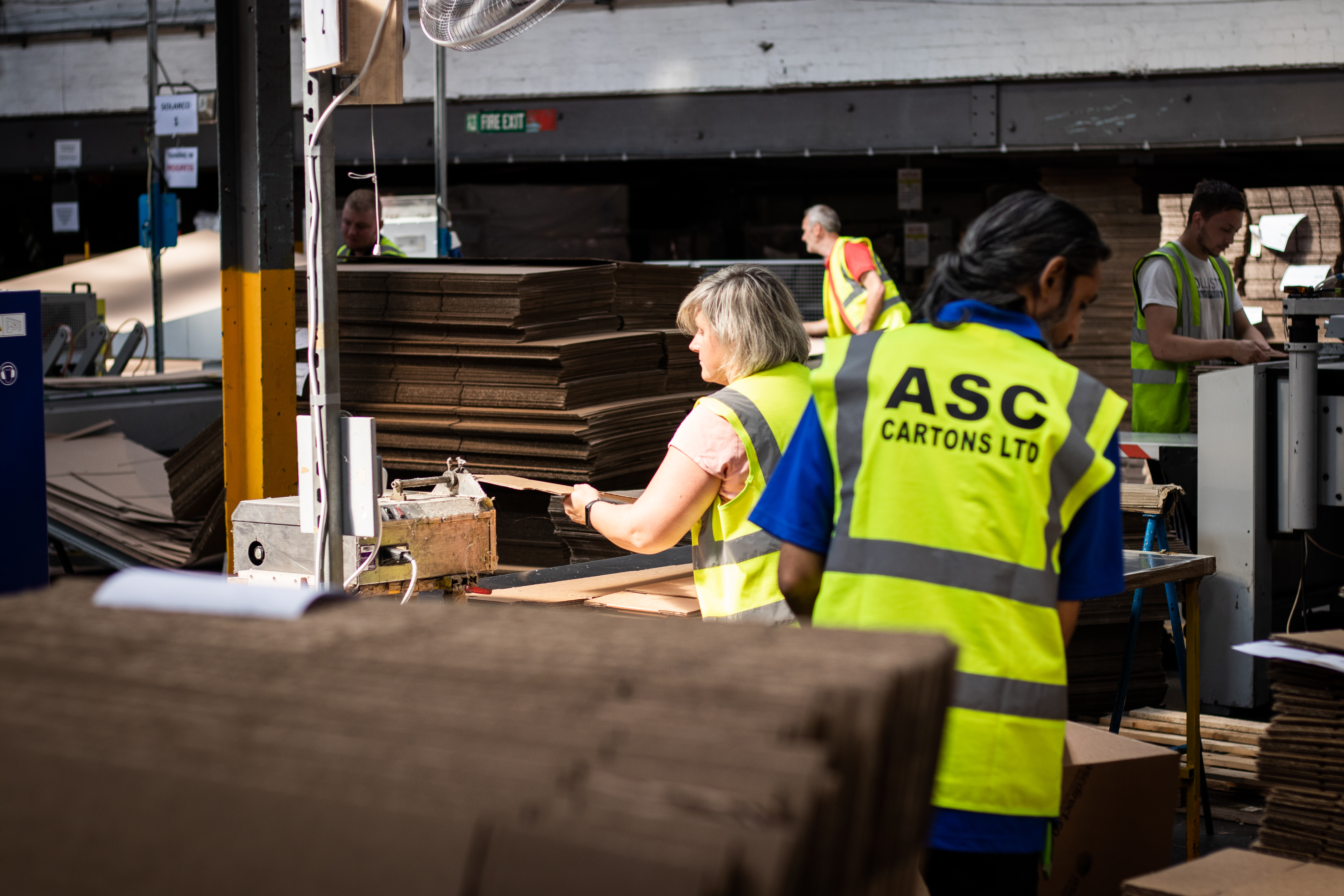 Multiple staff members building boxes, ASC Cartons LTD visible on back of vest