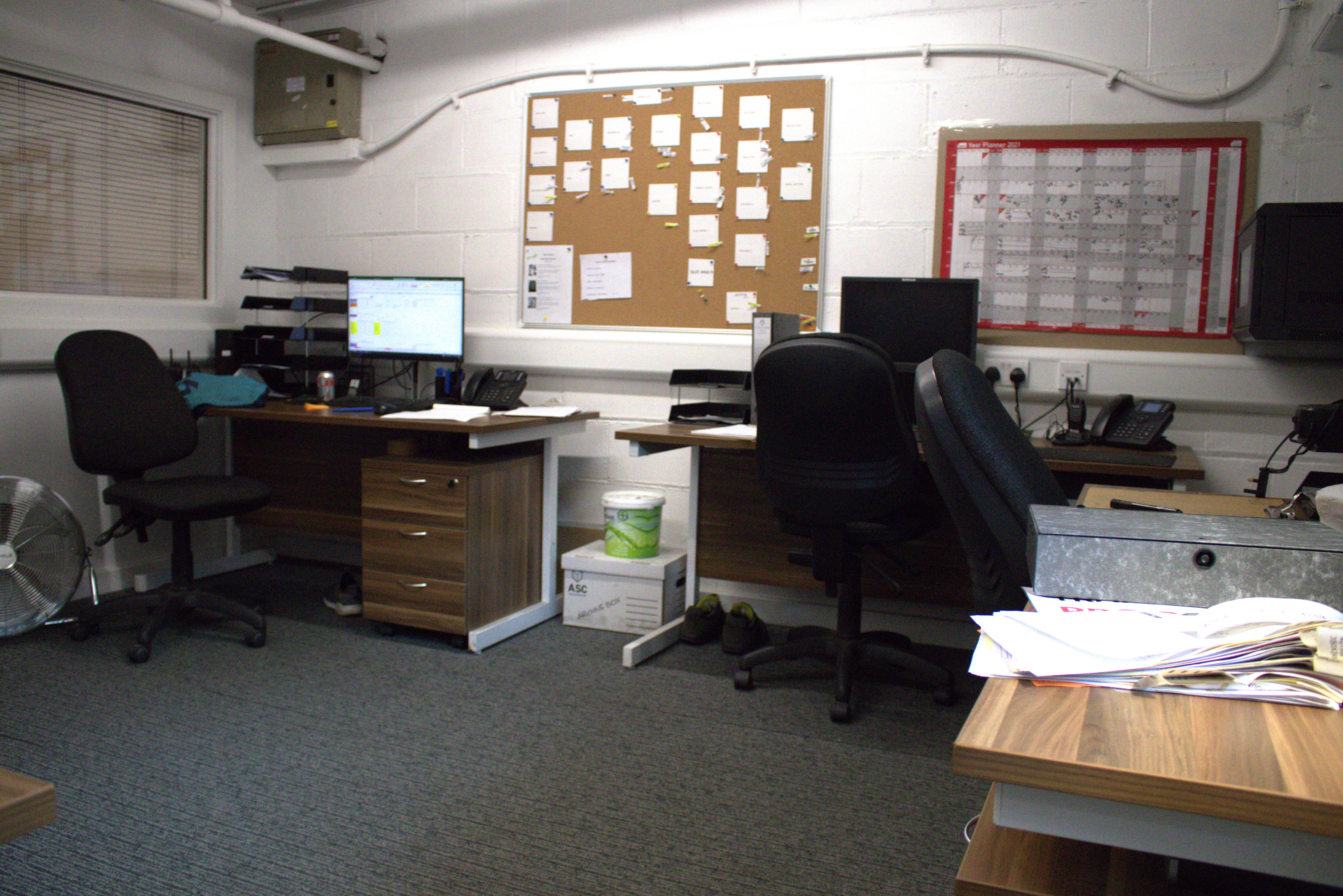 Office with no people showing lots of paper on desks and corkboard