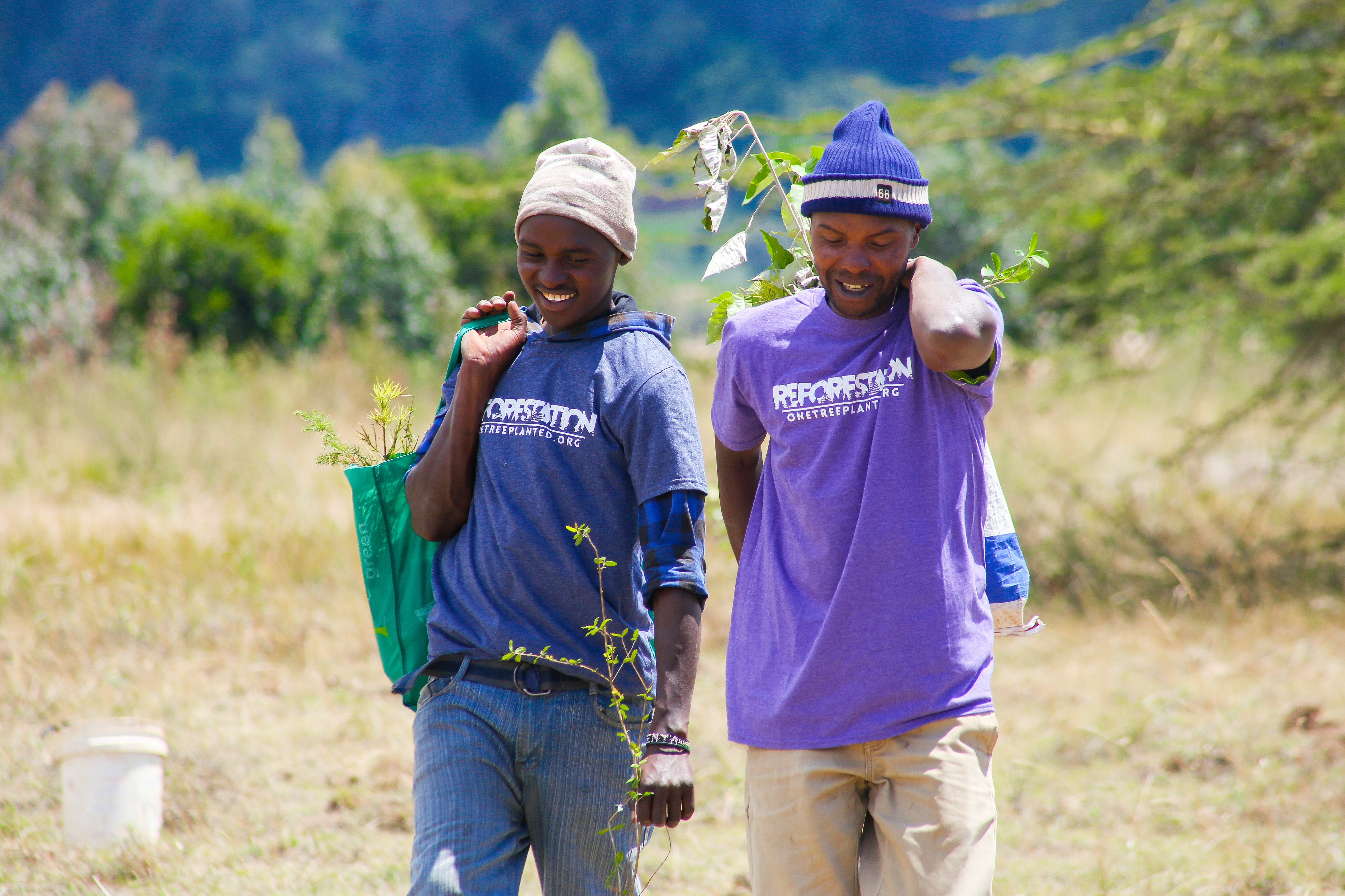 Two men smiling in the sun while carrying tree saplings for One Tree Planted