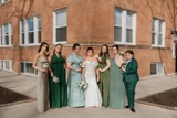A bride and her bridal party wearing different shades of green pose for a photo.