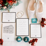 Flat lay with white sparkly bridal shoes, velvet green ring box with wedding rings styled with red florals and a full invitation suite.
