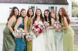 A bride and bridesmaids wearing different shades of green pose while holding multi-color wildflower bouquets.