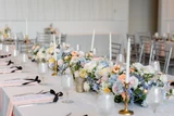 Multi-colored pastel floral runners line the center of a rectangle table at a wedding reception styled with gold candlesticks and place settings.