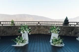 A minimal ceremony set up featuring four classic green and white floral meadows with a modern design sit on top two pillars draped in white fabric with another two floral meadows at the base of each pillar.