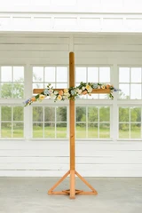 A multi-colored pastel garland is attached to a wooden cross for a minimal ceremony backdrop.
