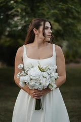 Bride looks off in the distance holding a white rose, hydrangea, lily of the valley, and larkspur bridal bouquet.