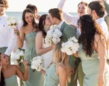 “Bride and groom kissing with bridesmaids and groomsmen holding white floral bouquets at a beach wedding celebration.