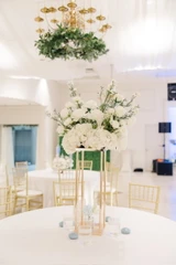 A white floral arrangement on top of a stand for an elevated centerpiece in the center of a round table at a wedding reception.