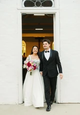 A bride holding a multi-color wildflower bridal bouquet walks arm in arm with her groom after their wedding ceremony.