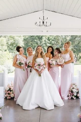 Bride holds a light pink and white bridal bouquet surrounded by her bridesmaids wearing light pink dresses and holding light pink and ivory bridesmaid bouquets.