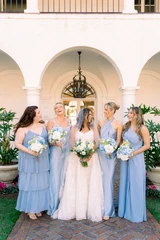 Bride in a wedding gown holding a blue and white bouquet posing for a picture with her bridesmaids wearing light blue dresses.