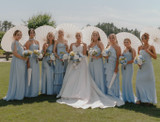 Bridal party wearing light blue dresses, holding umbrellas, and floral bouquets made of white and blue flowers with the bride in the middle holding a bouquet of white and blue flowers