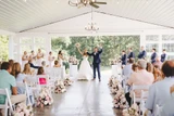 Bride and groom stand at the end of the aisle with the arms up in celebration while guest watch and light pink and ivory floral meadows line the aisle.