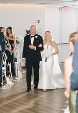 Bride walking down the aisle with her father holding a bouquet of all white roses, ranunculus, hydrangeas, and lily of the valley