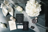 Detailed shot of wedding invitations and flowers featuring white ranunculus, hydrangeas, roses, and lily of the valley