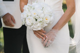 Close up shot of a bride holding her bridal bouquet made of all white roses, ranunculus, hydrangeas, and lily of the valley