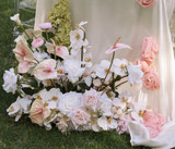 Ground-level floral arrangement featuring blush anthuriums, white orchids, pale pink roses, white hydrangeas, and soft green hydrangeas styled around draped ivory and blush fabric.