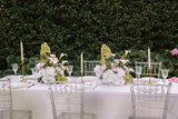 Elegant outdoor reception table styled with clear Chiavari chairs, gold taper candles, crystal glassware, and airy floral centerpieces featuring blush anthuriums, white calla lilies, white hydrangeas, and soft green hydrangeas.