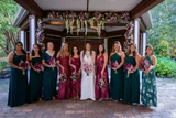 A photos of a bride and her bridesmaids wearing a mix of green and maroon holding bouquets featuring different shades of purple flowers.