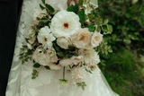 Close-up of a bridal bouquet featuring white and blush garden roses, white blooms, and greenery against a lace wedding gown backdrop.