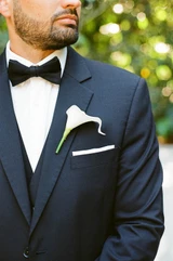 A white calla lily boutonniere is pinned to the lapel of a groom's navy blue tux.