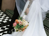 Bride holding a peach, blush, and ivory wedding bouquet against a flowing white gown.