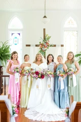 Bride and bridesmaids standing together indoors with cheerful pastel bouquets and coordinating ribbon details.
