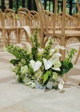 A classic green and white floral meadow with a modern design is placed next to a chair at an indoor wedding ceremony.
