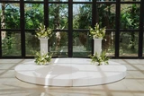 Four classic green and white floral meadows are placed on top and at the base of two white pillars for a minimal wedding ceremony backdrop.