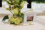A classic green and white vaseless centerpiece with a modern design is placed in the center of a round reception table next to a table number sign.