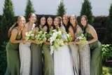A bride and her bridesmaids wearing different shades and prints of green pose with classic green and white bouqets.