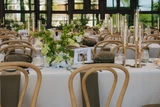 Rows of rectangle tables are photographed with classic green and white vaseless centerpieces with a modern design styled with brown napkins and tall gold candlesticks at an indoor wedding reception.