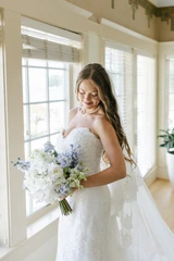 A bride looks down at her light blue and white bridal bouquet.
