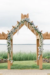A wedding ceremony arch is decorated with trailing light blue and white floral garlands at a waterfront coastal wedding.