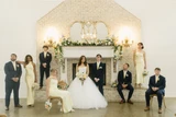 A bridal party poses in front of a fire place with multi-colored pastel floral garland draping off the edge of the mantel.