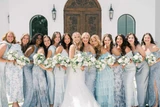 Bride and her bridesmaids wearing different shades and prints in light blue dresses pose for a photo holding bouquets made up of white florals and dark greenery.
