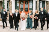 A wedding party walks towards the camera featuring red and pink floral bouquets.